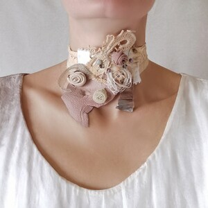 Peut inclure: Un collier ras de cou d&eacute;licat et superpos&eacute; en tissu, dentelle et cuir. Le collier pr&eacute;sente une vari&eacute;t&eacute; de textures et de couleurs, notamment le blanc, le beige et le brun. Le collier est orn&eacute; de petites fleurs d&eacute;licates et de perles.