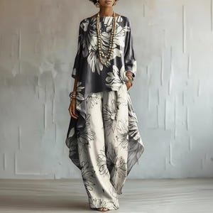May include: A two-piece outfit consisting of a loose-fitting, long-sleeved tunic top and wide-leg trousers. Both pieces feature a monochromatic black and white floral pattern. The tunic has an asymmetrical hemline, and the trousers are full-length.