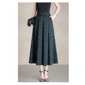 May include: A high-waisted midi skirt in a dark forest green and black floral pattern. The skirt features a structured waistband with a thin, dangling cord detail, side pockets, and a flared, A-line silhouette that falls below the knees.