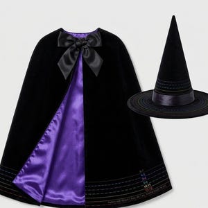 Puede incluir: Una capa de terciopelo negro con forro de satén morado, con un gran lazo de satén negro en el cuello. Se incluye un sombrero puntiagudo negro a juego con ala ancha y banda de satén. El dobladillo de la capa muestra marcas de guía de tallas.