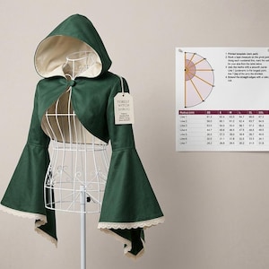 May include: A dark green shrug with a hood, bell sleeves, and cream-colored lining and lace trim. A tag reads Forest Witch Shrug. Beside it is a printed sizing chart with a diagram and a table of measurements in centimeters for sizes XS to XXL.