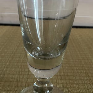 Op de afbeelding: Een helder glazen kelkglas met een brede, uitlopende kom die taps toeloopt naar een dikke, ronde steel en een ronde voet. Het glas heeft een glad, transparant oppervlak met een duidelijke horizontale rand die de kom scheidt.