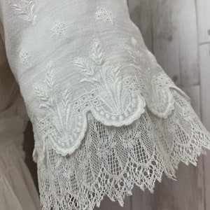 May include: White cotton blouse with a delicate floral embroidery pattern and a scalloped lace trim.