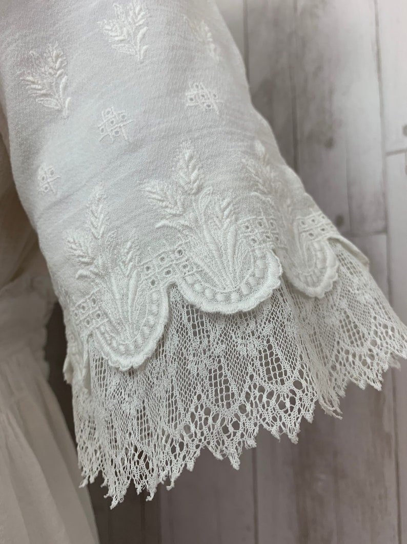 May include: White cotton blouse with a delicate floral embroidery pattern and a scalloped lace trim.