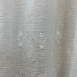May include: White fabric with a subtle embossed floral pattern. The fabric has a slightly textured surface and a soft, flowing drape.