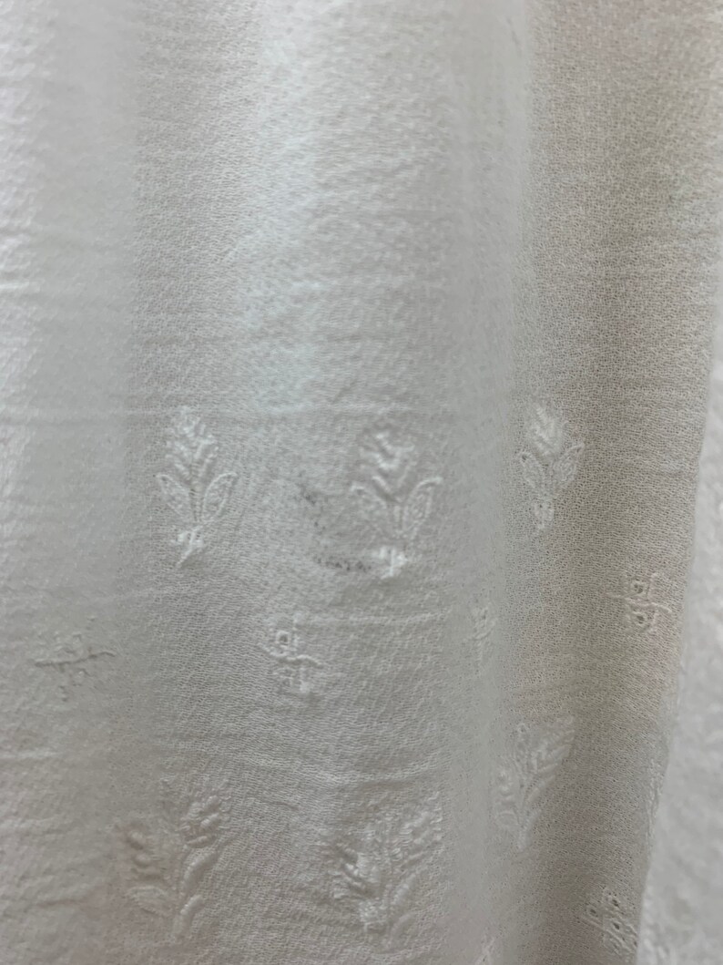 May include: White fabric with a subtle embossed floral pattern. The fabric has a slightly textured surface and a soft, flowing drape.