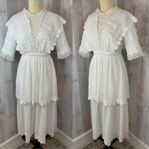 May include: A white cotton dress with a lace overlay and a tiered skirt. The dress has a scalloped neckline and short sleeves.