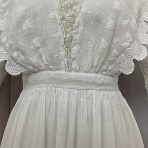 May include: White cotton dress with a lace trim and a scalloped neckline. The dress has a fitted bodice and a full skirt.