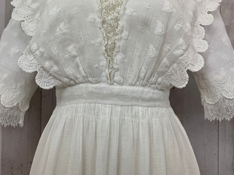 May include: White cotton dress with a lace trim and a scalloped neckline. The dress has a fitted bodice and a full skirt.