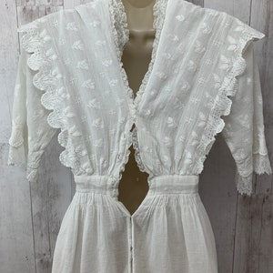 May include: A white cotton dress with a lace trim and a keyhole back. The dress has a v-neck and a fitted bodice. The skirt is full and flowing.