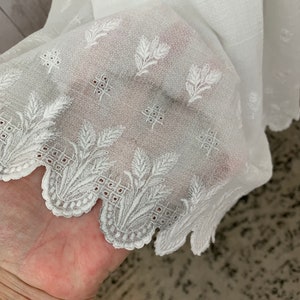 May include: White sheer fabric with an embroidered floral pattern and scalloped edge.