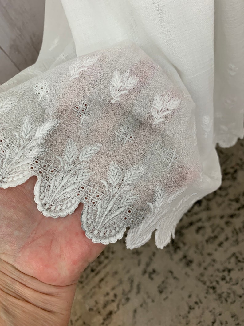 May include: White sheer fabric with an embroidered floral pattern and scalloped edge.