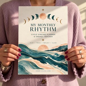 May include: A rectangular planner titled My Monthly Rhythm Cycle Syncing Planner & Energy Tracker. The cover features a moon phase graphic, a sun, and a landscape of teal and peach-coloured ocean waves with gold accents on a cream background.