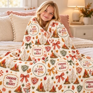 May include: A cream-colored throw blanket featuring a repeating pattern of autumn-themed illustrations, including temples, bows, and shields with the text "CTR" and "CHOOSE THE RIGHT" and "I AM a child OF GOD" in red, green, and orange hues.