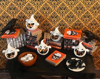 Könnte beinhalten: Ein Halloween-Tischset mit weißen, geisterförmigen Süßigkeitenschalen, gefüllt mit Süßigkeiten, schwarzen Raben und Stapeln von Büchern mit dem Wort "Halloween" auf den Rückseiten.