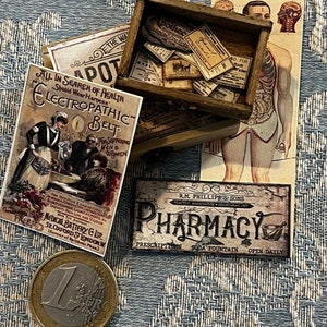May include: A collection of miniature vintage apothecary and medical ephemera. Includes a wooden box with tiny labels, a pharmacy sign, an advertisement for an "Electropathic Belt", and a euro coin. The items are arranged on a patterned blue surface.