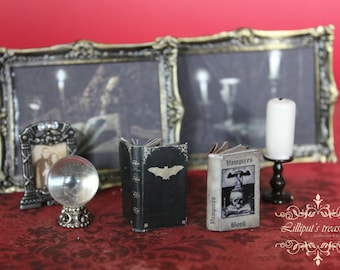 May include: A miniature scene with two framed pictures, a crystal ball, and two small books. The books are titled "Vampires" and "Book". The scene is set on a red surface with a decorative border.