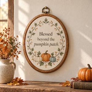 May include: An oval wall hanging featuring a wooden frame and a fabric center with the text Blessed beyond the pumpkin patch. The design includes a printed wreath of green leaves, small berries, and three pumpkins in white, orange, and blue.
