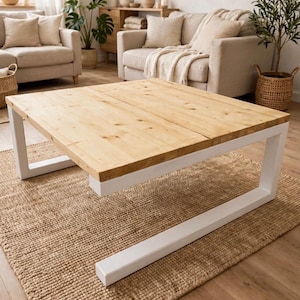 Könnte beinhalten: Ein quadratischer Couchtisch mit einer hellen Naturholzplatte und einem stabilen weißen Metallrahmen. Der Tisch hat ein niedriges Design mit dicken, rechteckigen Beinen, die sich entlang des Bodens erstrecken und eine stabile Basis bieten.