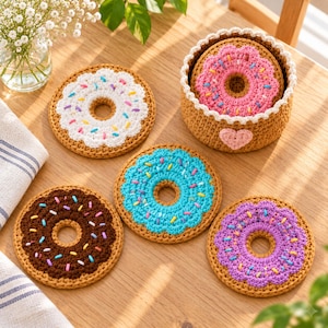 Könnte beinhalten: Ein Set aus fünf gehäkelten Untersetzern in Donut-Form in Braun, Weiß, Pink, Blau und Lila mit bunten Streuseln, dazu ein passender runder gehäkelter Aufbewahrungskorb mit einem kleinen rosa Herz an der Seite.