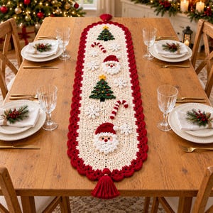 Puede incluir: Un camino de mesa de ganchillo color crema con un borde festoneado rojo y borlas rojas en los extremos. El camino presenta motivos navideños aplicados que incluyen caras de Papá Noel, árboles de Navidad verdes con estrellas y copos de nieve.