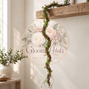 May include: A long, twisted brown vine garland adorned with small green leaves, hanging vertically from a wooden shelf. Behind the vine is a circular logo featuring a floral arrangement of white and pink roses with the text Gloom Petals.