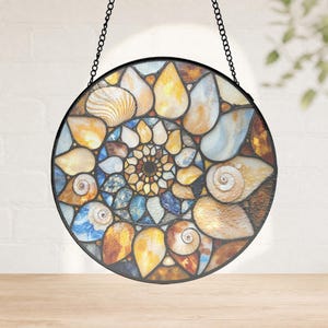 Könnte beinhalten: Ein runder Buntglas-Suncatcher mit einem spiralförmigen Ammoniten-Fossil-Muster. Das Design besteht aus zahlreichen einzelnen Glasstücken in Bernstein-, Blau- und Weißtönen, die durch dunkle Metalllötungen zusammengehalten und an einer schwarzen Kette aufgehängt sind.