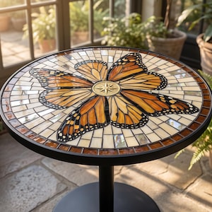 May include: A round side table featuring a mosaic tabletop with a central gold compass rose surrounded by orange and black monarch butterfly wing patterns. The mosaic is composed of small glass tiles in cream, brown, and orange, set in a black frame.