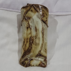 May include: A cylindrical ceramic vase featuring a glossy finish with a cream-colored base and dark brown, swirling, organic-looking streaks that wrap around the exterior surface, creating a textured and marbled appearance throughout.