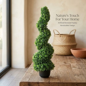Peut inclure: Un topiaire en buis artificiel en forme de spirale, planté dans un pot noir. Le texte indique : Nature's Touch For Your Home, Artificial Boxwood Topiary, Handcrafted Design. La plante présente des feuilles denses, petites et vert vif.
