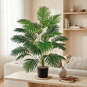 Peut inclure: Une grande plante palmier artificielle dotée de frondes plumeuses vert vif s'étendant vers l'extérieur depuis une tige centrale. La plante est placée dans un pot cylindrique noir simple, rempli de petites pierres décoratives claires à la base.