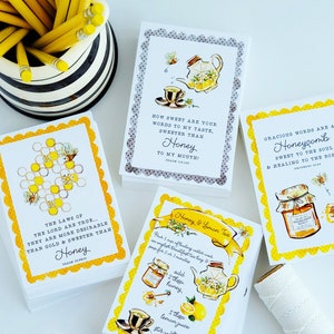 May include: A stack of white cards with yellow scalloped edges and watercolor illustrations of honey-related themes. The cards feature text about honey and tea, with images of honeycombs, teacups, and teapots. A black and white striped container with yellow pencils is in the background.