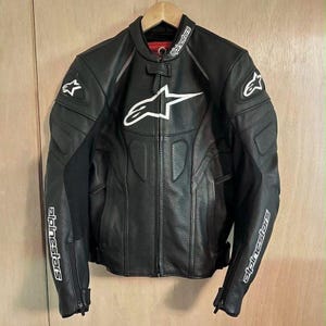 Może przedstawiać: Czarna skórzana kurtka motocyklowa z białym logo Alpinestars na klatce piersiowej, kołnierzu i rękawach. Kurtka posiada perforowane panele skórzane z przodu, centralny zamek błyskawiczny oraz zapięcie kołnierza na zatrzask.