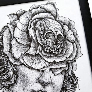 May include: A black and white stippled ink drawing in a black frame depicting a human face with a large rose blooming from the forehead. A detailed human skull is nestled within the center of the rose petals, obscuring the upper portion of the face.