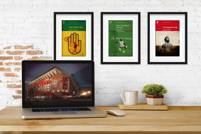 May include: Three framed prints with a sports theme. The prints feature a hand with an eye, a soccer player, and a soccer player with a crown. The prints are hanging on a white brick wall above a laptop computer.