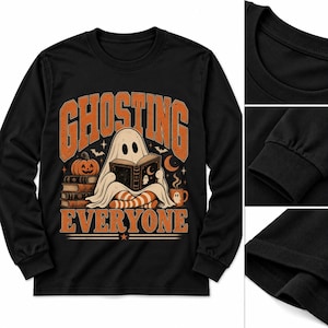 May include: A black long-sleeve shirt featuring a graphic of a ghost reading a book, a pumpkin, and a mug. The text reads GHOSTING EVERYONE in orange block letters. The design includes stars, bats, and a crescent moon on a black background.