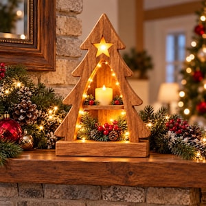 Peut inclure: Une décoration en bois en forme de sapin de Noël avec une étoile découpée au sommet, dotée d'une petite étagère portant une bougie pilier blanche, illuminée par des guirlandes lumineuses et ornée de branches de pin et de baies rouges.