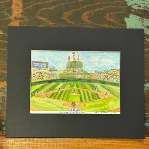 Puede incluir: Una pintura en acuarela con paspartú que muestra un campo de béisbol con jugadores en uniformes azules en el diamante. El marcador muestra el texto Cincy 150 Years y 150. El margen inferior presenta el texto escrito a mano My View Of Wright Field.
