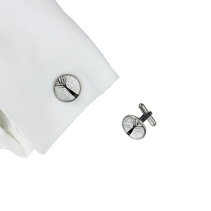 May include: A pair of silver cufflinks with a black and white image of a tree on each cufflink.