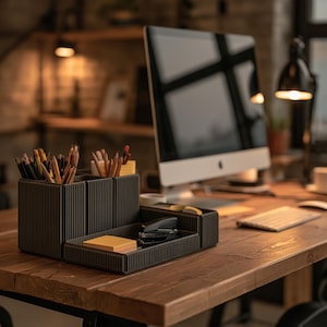 May include: A dark gray modular desk organizer with a ribbed texture, featuring multiple vertical compartments for pencils and pens, and a shallow tray section containing a black stapler and a stack of square yellow sticky notes.