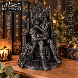 May include: A dark gray 3D printed figurine of two figures sitting on a gothic throne. One figure sits on the lap of the other, with both figures wearing boots and textured clothing. The throne features a pointed arch back and a star emblem.