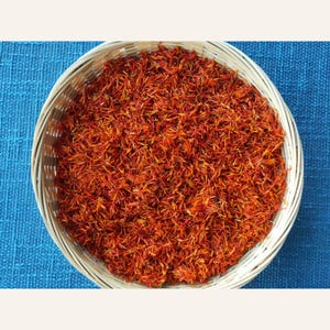 May include: A round, light-colored woven basket filled with a large quantity of dried, vibrant red and orange saffron threads. The thin, delicate filaments are densely packed, creating a textured surface of deep crimson and golden yellow hues.