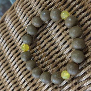 May include: A circular bracelet composed of numerous matte, dark brown, spherical beads interspersed with three smooth, translucent, bright yellow beads. The beads are strung together in a continuous loop, creating a simple and uniform design.