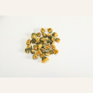 May include: A cluster of dried yellow chrysanthemum flowers. Each individual flower head is small, rounded, and tightly packed with golden-yellow petals, showing a slightly withered texture from the drying process, arranged in a loose pile.