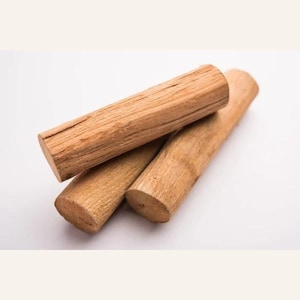 May include: Three cylindrical pieces of light brown sandalwood arranged in a small stack. Each piece features a natural wood grain texture with visible longitudinal lines and a rough, fibrous surface on the cut ends of the logs.