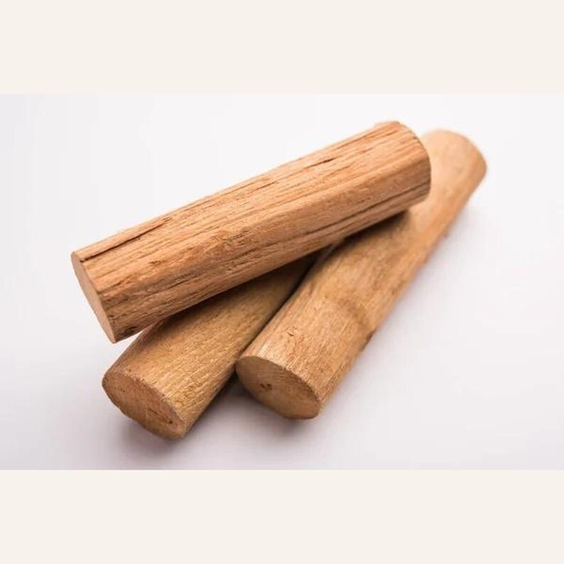 May include: Three cylindrical pieces of light brown sandalwood arranged in a small stack. Each piece features a natural wood grain texture with visible longitudinal lines and a rough, fibrous surface on the cut ends of the logs.