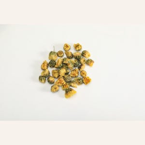 May include: A cluster of dried yellow chrysanthemum flowers. Each individual flower head is small, rounded, and tightly packed with golden-yellow petals, showing a slightly withered texture from the drying process, arranged in a loose pile.