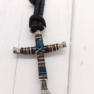 May include: A colorful, multi-colored, wire-wrapped horseshoe cross keychain. The cross is made of metal and is attached to a black cord with a blue accent.