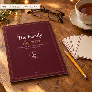 Può includere: Un libretto bordeaux intitolato The Family Reporter con il logo di una sedia a dondolo bianca, accompagnato da un mazzo di carte color crema vuote e una matita gialla. Il testo indica 48 carte domanda, un pass stampa ed età 6 a 98.