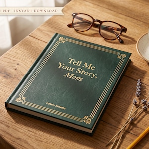 Puede incluir: Un diario de tapa dura de color verde oscuro con letras doradas que dicen Tell Me Your Story, Mom y Porch Stories. El libro presenta un borde decorativo dorado, acompañado de gafas de montura marrón, una taza de cerámica y un lápiz amarillo.